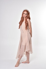 full length portrait of a pretty, fairy girl wearing a nude flowy dress and crystal crown. Standing and dancing pose against a grey studio background.