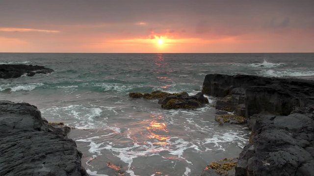 Hawaii sunset with ocean waves crashing against rugged black lava