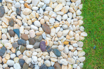 Colorful small pebbles or stone texture in garden with difference color and small green grass texture on the right.