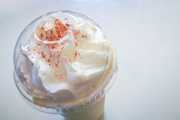 White whip cream and little chocolate on ice coffee in plastic cup or glass on white table.