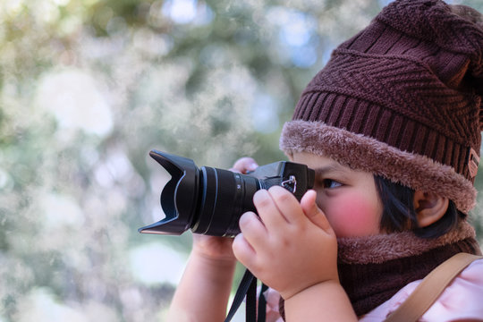 Portrait of a cute little girl in Wool hat taking a picture with digital camera at the weather is cold on blurred background