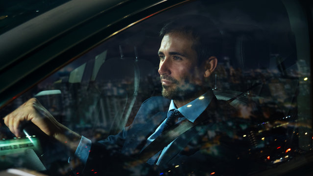 An young handsome businessman driving a modern car in center of the city by night. Concept of business, success, traveling, luxury