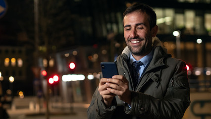 An young man is using mobile phone in a center of the city by night.