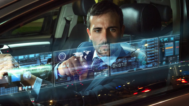 A handsome businessman is using an application of self pilot on a futuristic screen with augmented reality holograms  before a drive a car.