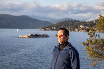 Fototapeta premium Portrait of an Adventurous Latin Man outside in nature during a cloudy and sunny sunset. Taken in Lighthouse Park, Horseshoe Bay, West Vancouver, BC, Canada.