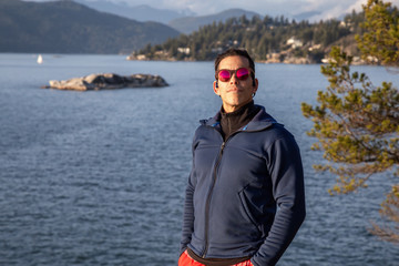 Fototapeta premium Portrait of an Adventurous Latin Man outside in nature during a cloudy and sunny sunset. Taken in Lighthouse Park, Horseshoe Bay, West Vancouver, BC, Canada.