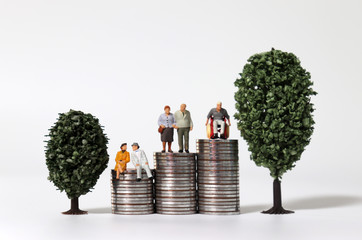 Old-age miniature people on a pile of coins between miniature trees.