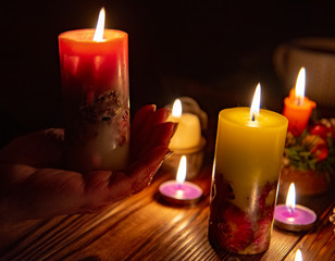 Burning candle on the palm compared to other candles on wooden background.