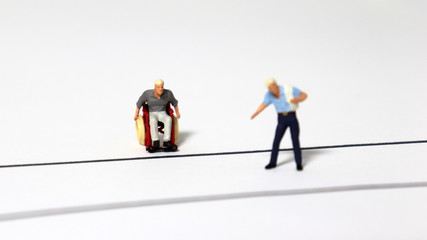 A miniature man in a wheelchair and a miniature man standing on the road.