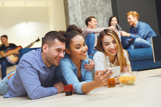 Group of friends having party indoors fun together lying on the floor taking selfies