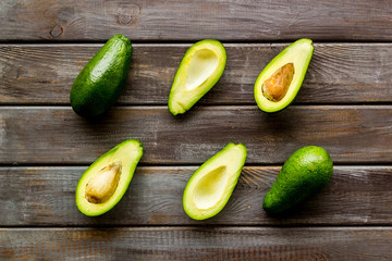 Avocado pattern - halfs of fruit - on dark wooden background top view