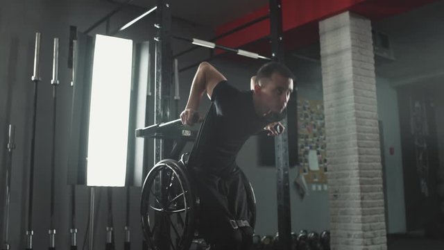 Workout, young disabled athlete in wheelchair performs push-ups on bars, gym training and physical activity.