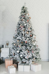 Beautiful glowing white snow-covered Christmas tree in the home interior. Vertical color photography
