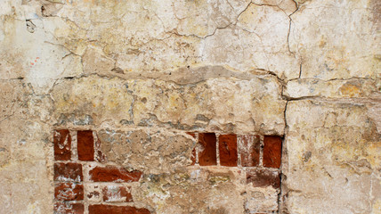 texture of concrete wall of an abandoned old house under crumbling and peeling beige stucco with cracks