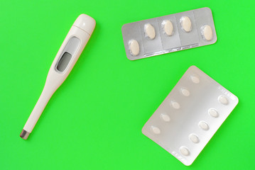 Pills and thermometer on a green background. Flat lay, top view, copy space. Pharmacy concept