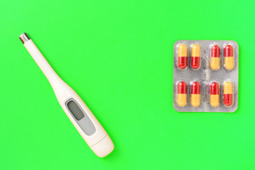 Pills and thermometer on a green background. Flat lay, top view, copy space. Pharmacy concept