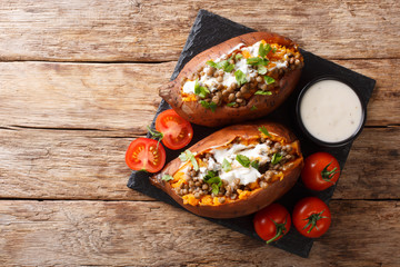 Rustic style baked sweet potato stuffed with lentils, garlic and parsley served with sour cream closeup on a slate board. Horizontal top view