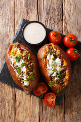 Tasty baked sweet potato with lentils and topped with sour cream close-up on a plate. Vertical top view