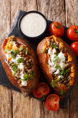 Baked sweet potato stuffed with lentils and topped with sour cream close-up on a plate. Vertical top vie