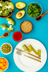Diet program concept. Empty plate, measure tape and vegetables on blue background top view