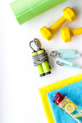 Fitness background - dumbbells, jump rope, sport carpet, water bottle - on white top-down copy space