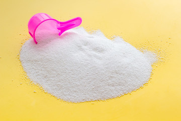 Household chemicals. Washing powder in plastic spoon on yellow background
