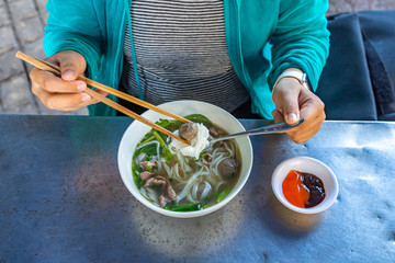 Female traveler eating famous Vietnamese food- Pho beef noodle soup