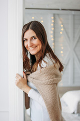 Beautiful smiling young woman dark long hair girl wearing in cozy knitted cardigan looking from door at home