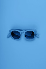 Classic blue color of 2020 sun glasses. Monochrome minimal fashion flat lay.