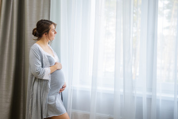 happy pregnant woman sitting on bed and touching her belly at home