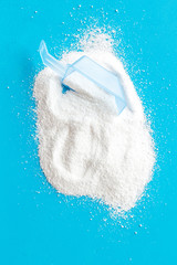 Washing powder in plastic spoon on blue background top view