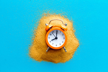 Waste of time concept. Clock on sand on blue background top-down copy space