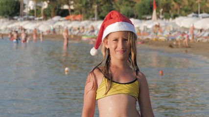 Little adorable girl in red Santa hat having fun at beach.
