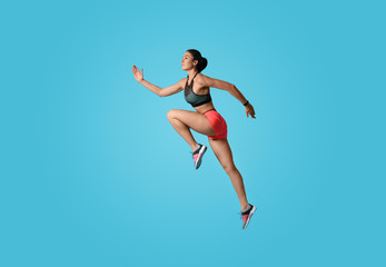 Fototapeta na wymiar Athletic young woman running on light blue background, side view