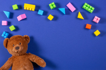 Baby kids toys background. Brown teddy bear and colorful wooden blocks and cubes on blue background. Top view