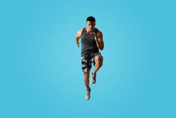 Fototapeta na wymiar Athletic young man running on light blue background