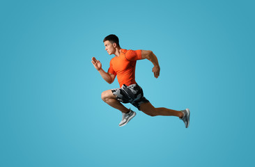 Obraz na płótnie Canvas Athletic young man running on light blue background, side view