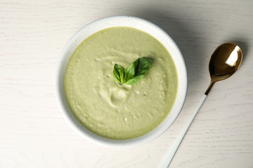 Delicious broccoli cream soup served on white wooden table, flat lay