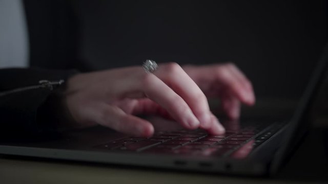 Woman's hands typing fast on a laptop keyboard. Dark environment.