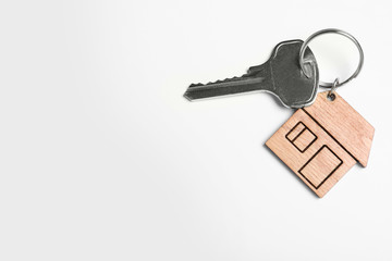 Key with trinket in shape of house isolated on white, top view. Real estate agent services