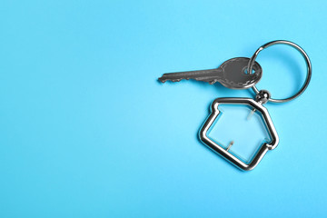 Key with trinket in shape of house on light blue background, top view and space for text. Real estate agent services