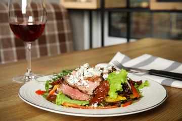 Delicious salad with roasted meat and vegetables served on wooden table indoors. Space for text