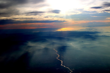 spectacular sunset seen from an airplane with the sun reflecting off a river and the  mountains in the background