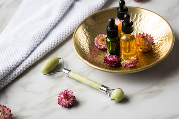 Massage Steinroller mit Naturkosmetik Beauty Öl Serum Flaschen an Handtuch, Gold Metall Schale und...