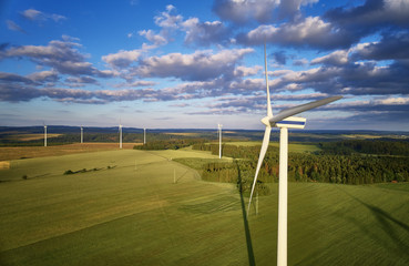 Aerial view of wind turbine farm. Wind power plants in green landscape against sunset sky with...