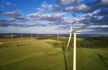 Aerial view of wind turbine farm. Wind power plants in green landscape against sunset sky with clouds. Aerial, drone inspection of wind turbine. © Martin Mecnarowski