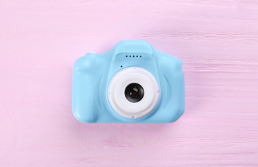Light blue toy camera on pink wooden background, top view