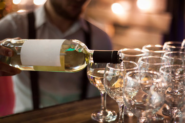 The waiter pours white wine into wine glasses. Close-up on glass.