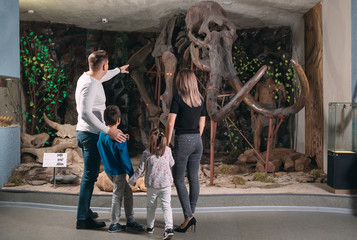 Family in the Museum. A family stands in front of a mammoth skeleton in the Museum of paleontology. - obrazy, fototapety, plakaty