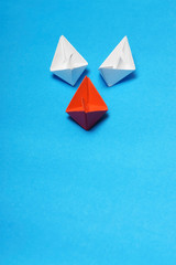 Leadership Concept: Red paper ship among white with a blue background and copy space